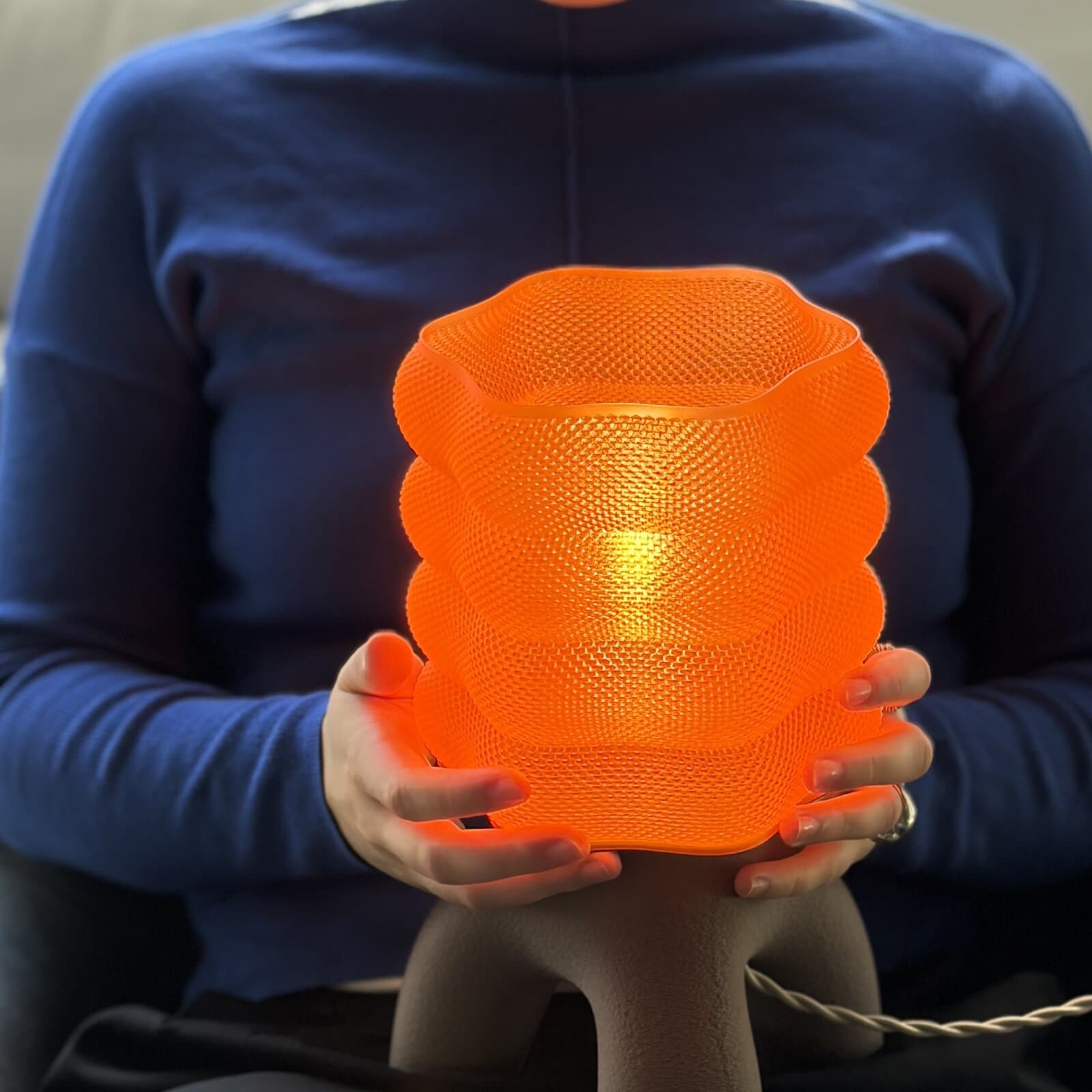 An Umbray lamp with an orange shade, lit, cradled in two hands