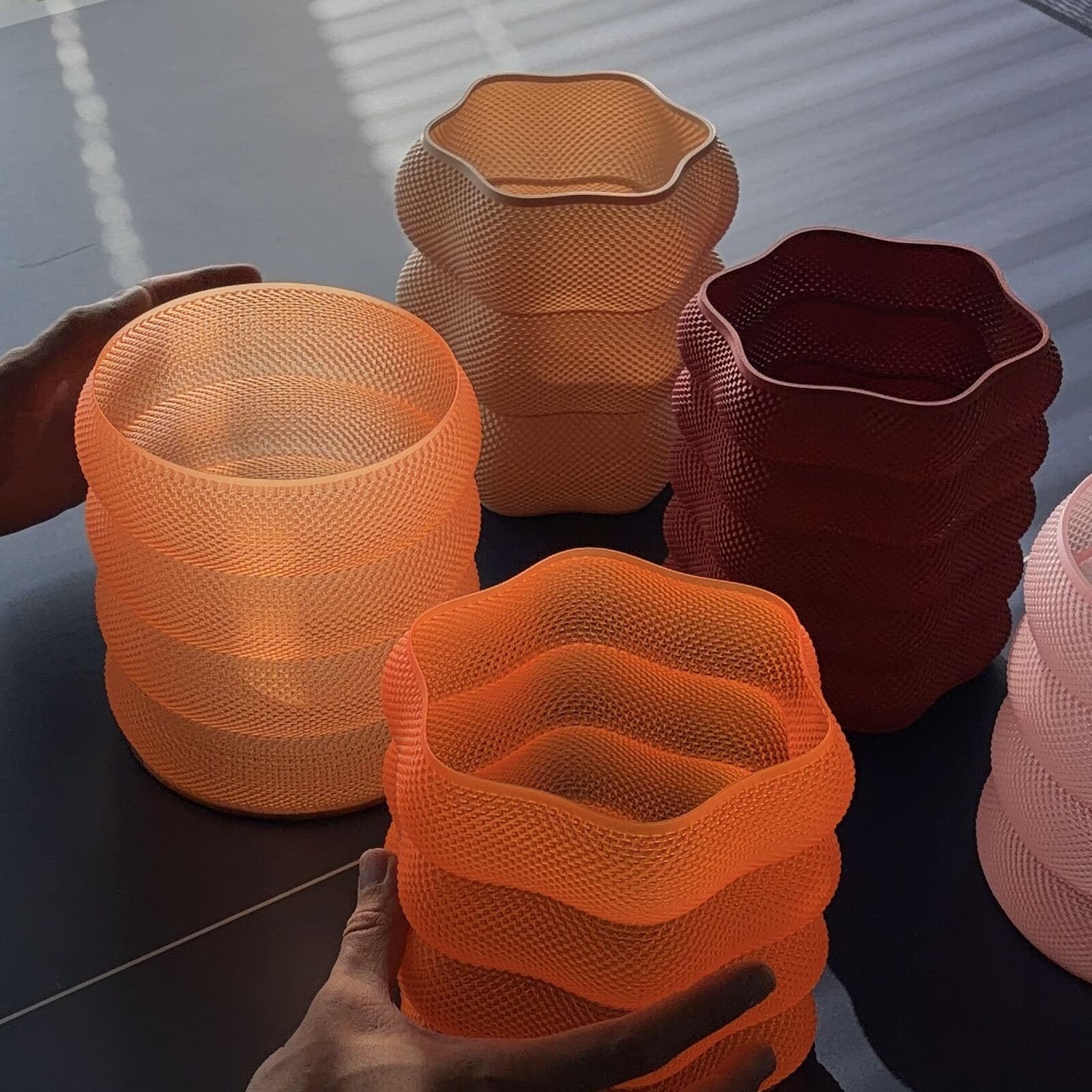 Four freshly printed Umbray lamp shades in different colors on a studio table, a hand reaching for one